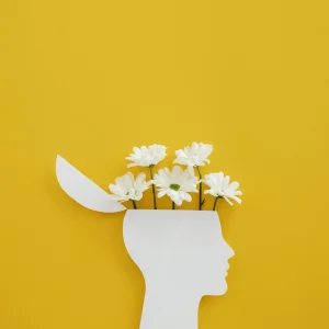 Sagoma di una testa da cui sopra sbucano fiori che sbocciano grazie a una mentalità positiva e amorevole.